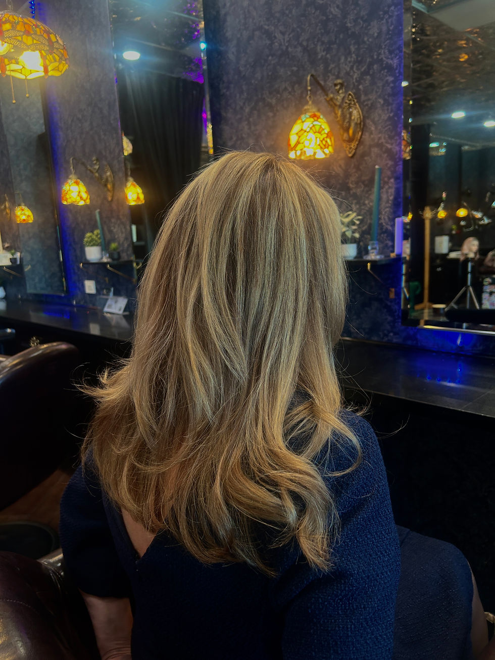 Medium-length blonde hair with soft layers and blended highlights styled in loose movement and volume inside a luxury salon setting.