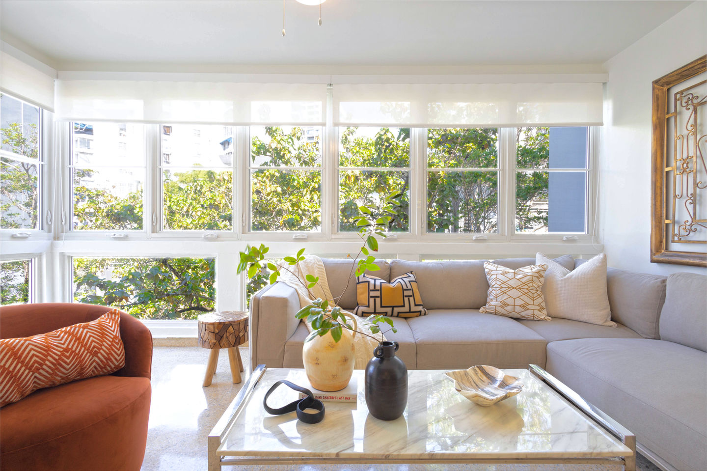 Spacious living room featuring a comfortable sofa and accent chair with a view of lush trees through floor-to-ceiling windows in Villa Maria, vacation rental in Miramar, San Juan Puerto Rico. For vacation, corporate stay, home away from home. Walking distance to restaurants, cafes, parks.
