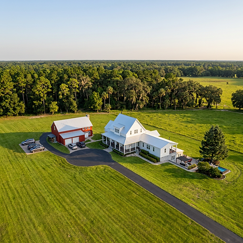 Aerial view of a white farmhouse and red barn in a field.