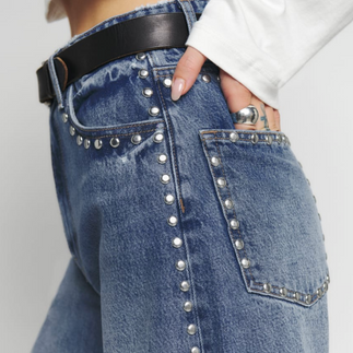 A close up of a model wearing studded denim jeans