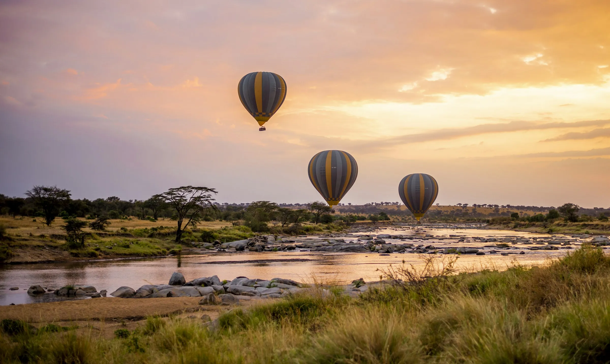 Hot air balloons over a river at sunrise