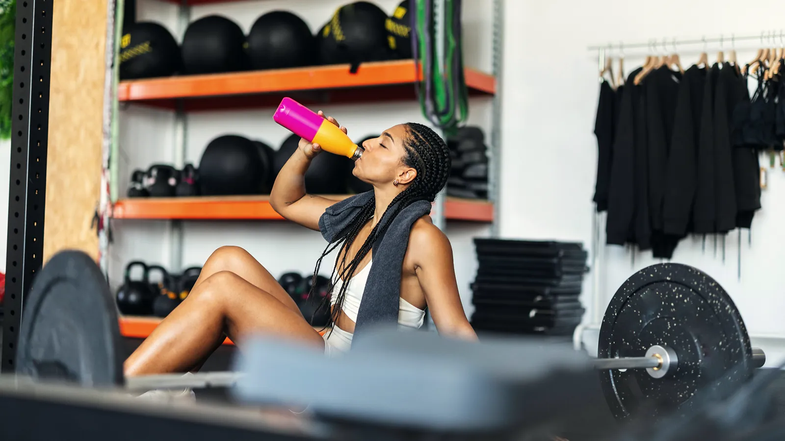 Woman taking a water break on the floor of a gym between sets