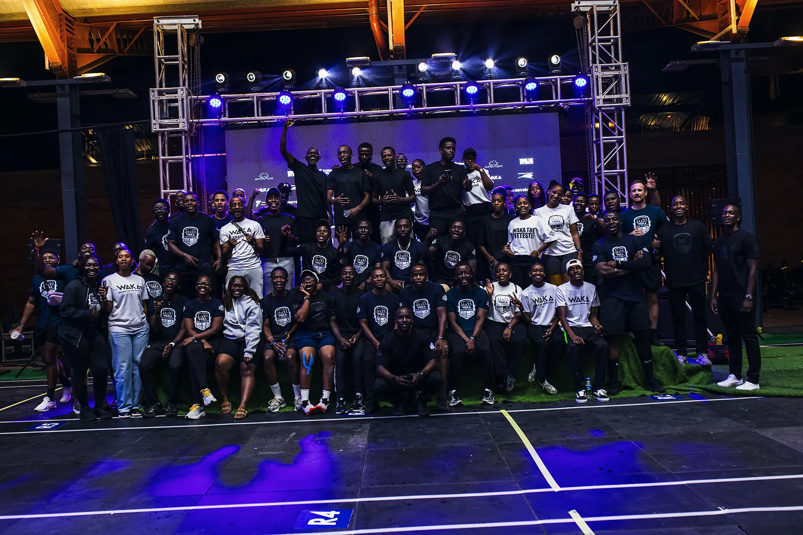 Event team, judges and athletes gathered on stage under blue lights after a fitness competition