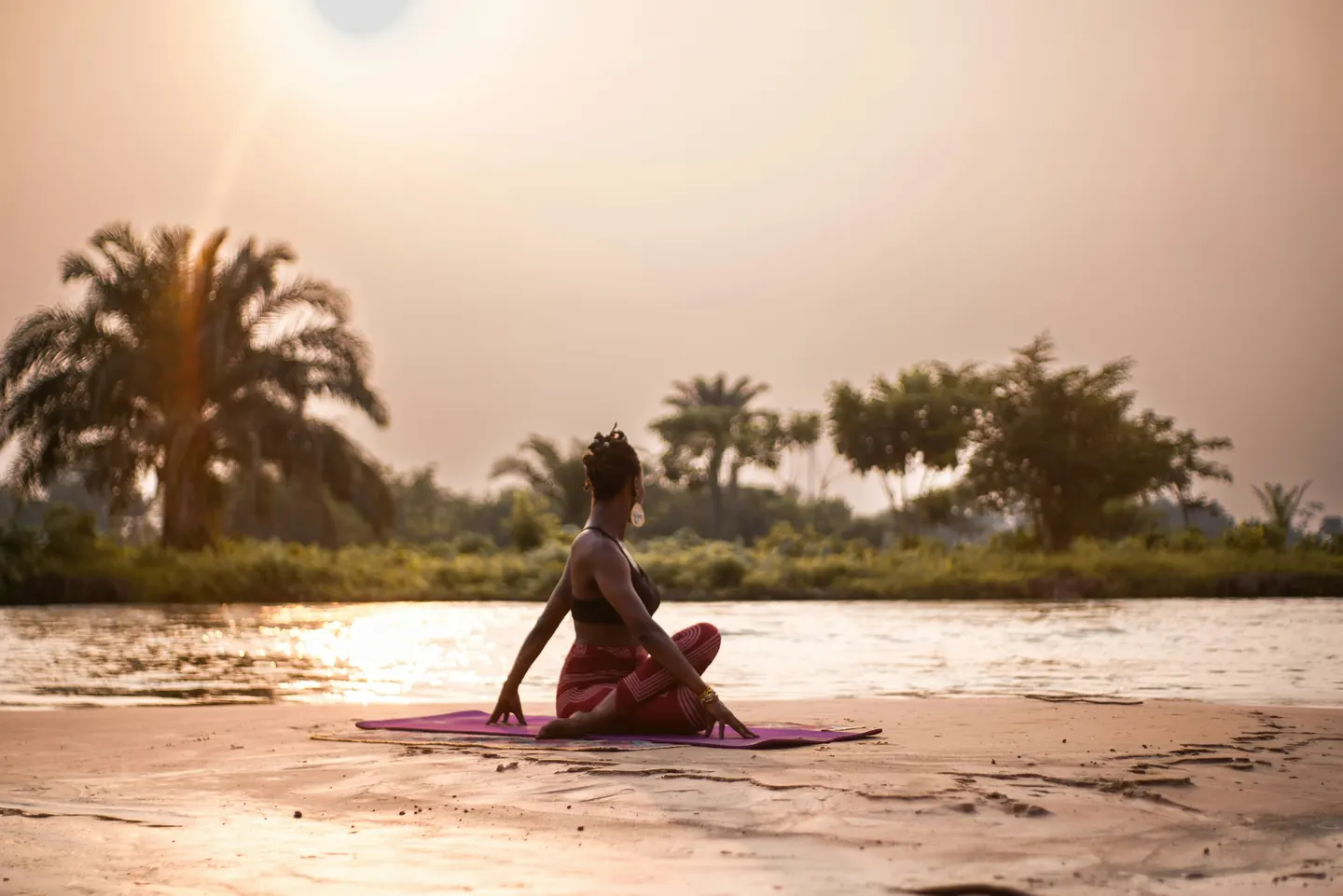 Woman practising yoga by the water at sunset