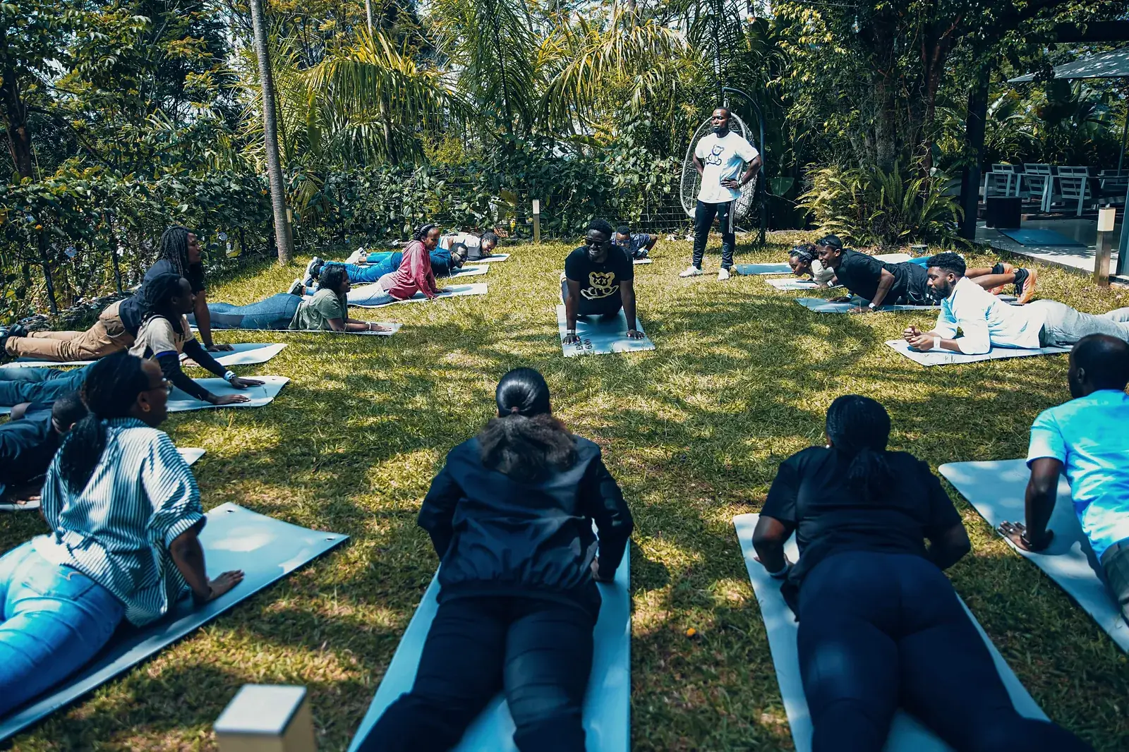 Group stretching on mats in a garden while a coach looks on