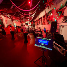 A wide view of a corporate holiday party venue with guests, festive ceiling streamers, and a Karaoke 2 Go digital display.