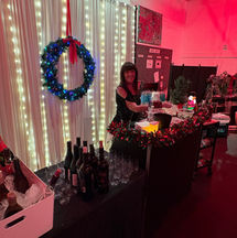 A professional bar setup at a holiday event featuring wine, champagne on ice, and a festive wreath backdrop.