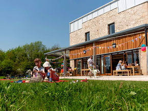 2 children sat on the grass outside mount cook adventure centre. Sunny day, blue sky.