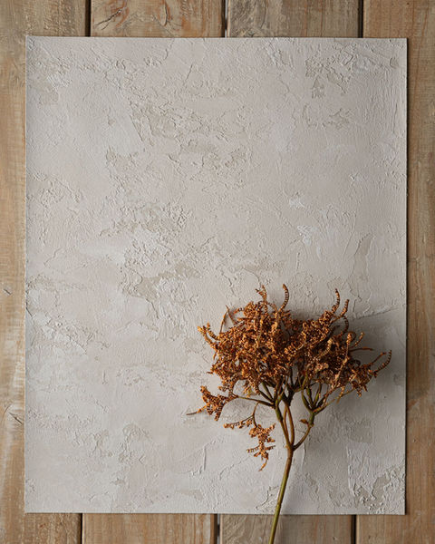 A closeup of Vacarda’s rustic nude art wall plaster with a flower branch on a wooden surface.