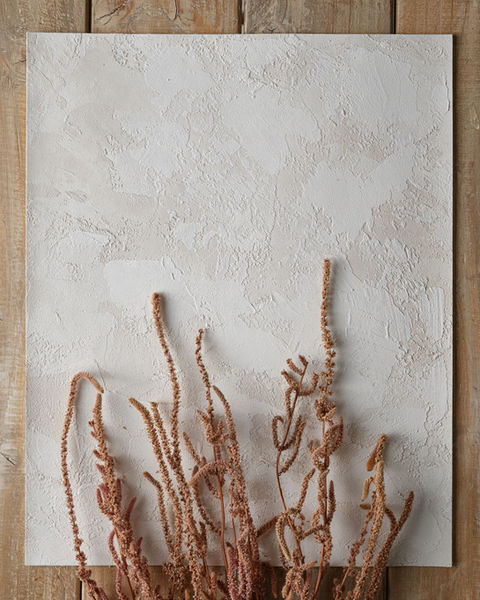 A closeup of Vacarda’s rustic neutral art wall plaster with wild heather flowers on a wooden surface.