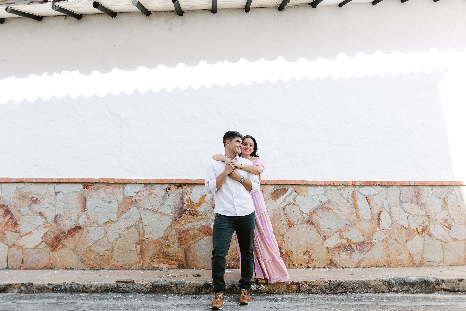 Pareja abrazándose durante su sesión de preboda en Mesa de los Santos, Bucaramanga. Ambos visten camisas blancas mientras se miran con ternura bajo un árbol iluminado por la luz suave del atardecer. Fotografía natural y emotiva capturada por Johan Rey, fotógrafo de bodas en Colombia.