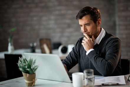 smiling-businessman-using-laptop-contemplating-while-working-his-desk-office.jpg