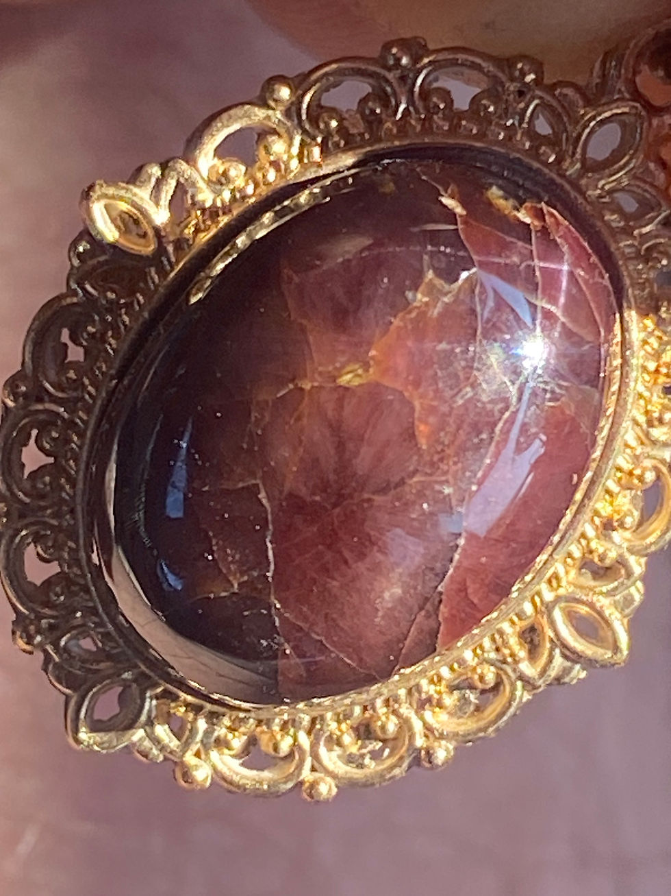 Thumbnail: Close-up of a Garnet Rhodolite pendant set in an ornate gold frame against a textured wood background.