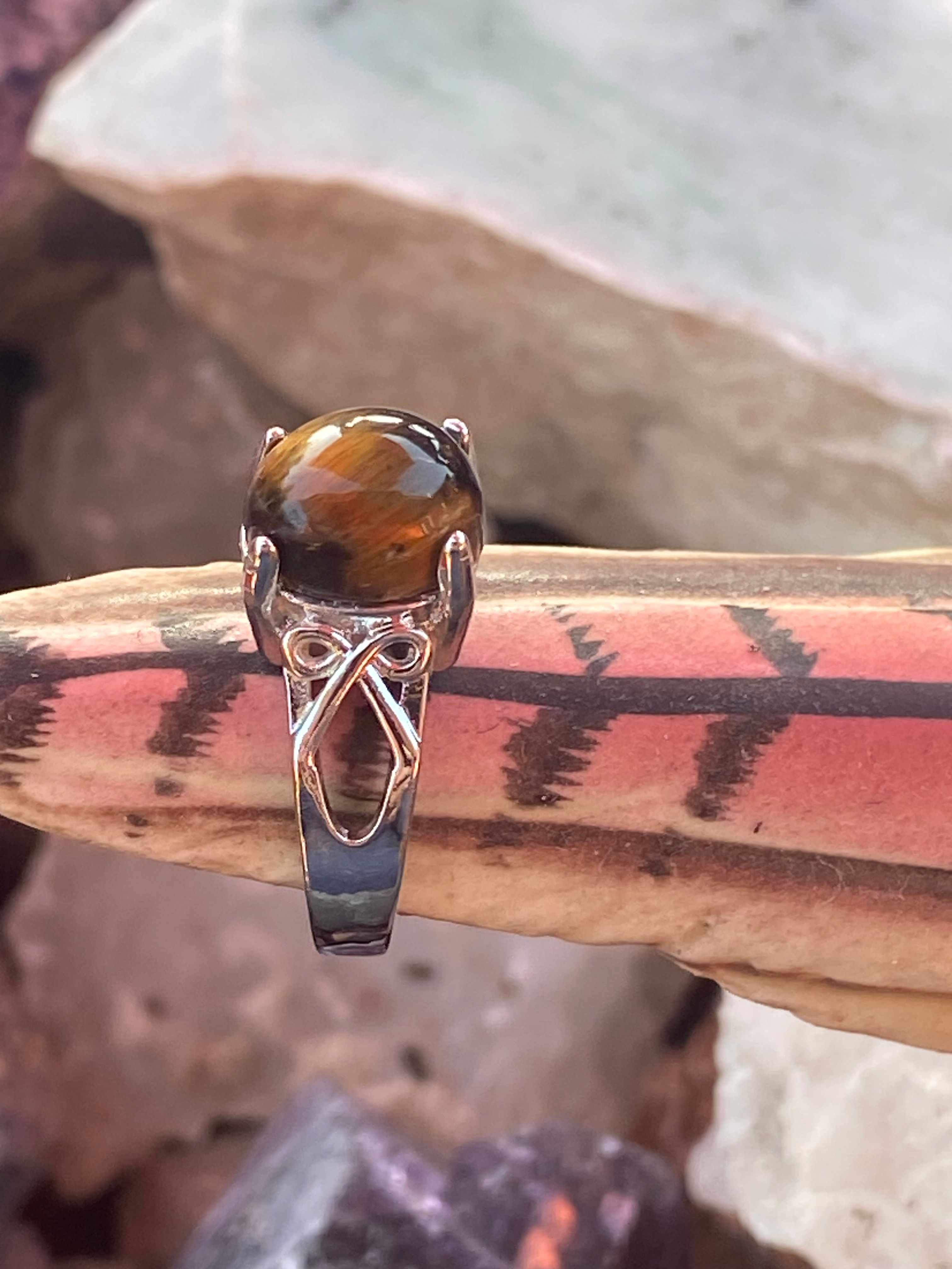 Close-up of a Tiger Eye gemstone set in a silver-plated ring on a decorative background.
