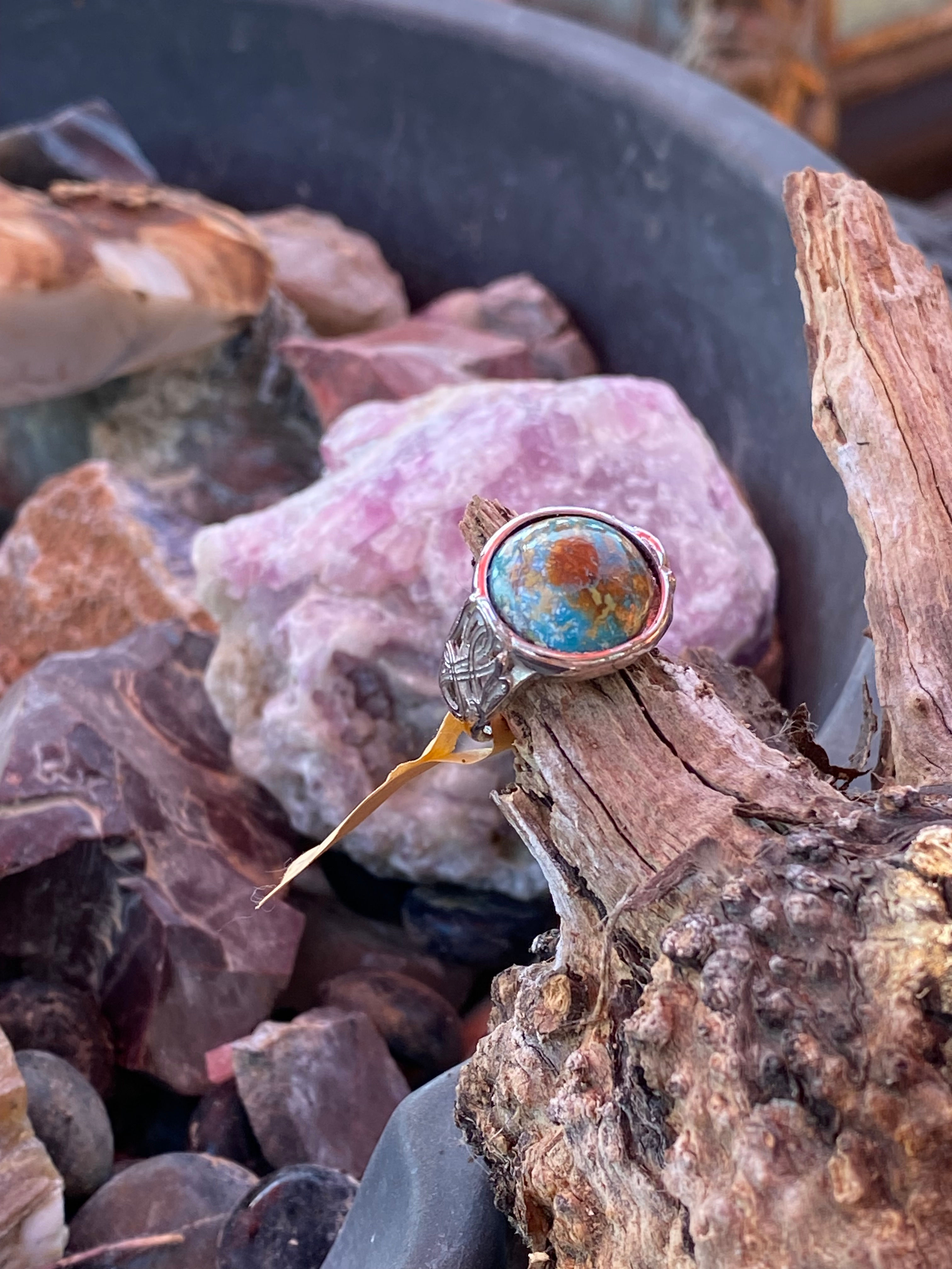 Untreated turquoise ring on a silver plated setting displayed on a rustic wooden background with colorful crystals.