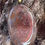 Thumbnail: A close-up of a Moss Agate pendant showcasing its intricate green and red inclusions, mounted on a gold-toned bail, resting a