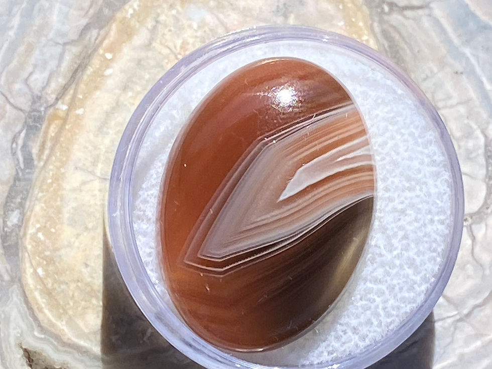 Thumbnail: Polished Banded Agate gemstone with soft cream and white bands resting on a natural stone background.