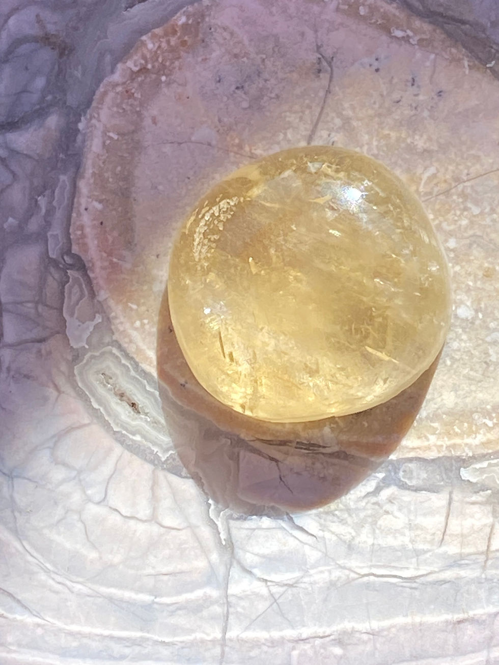 Polished Yellow Citrine gemstone with a golden glow resting on a natural stone background.