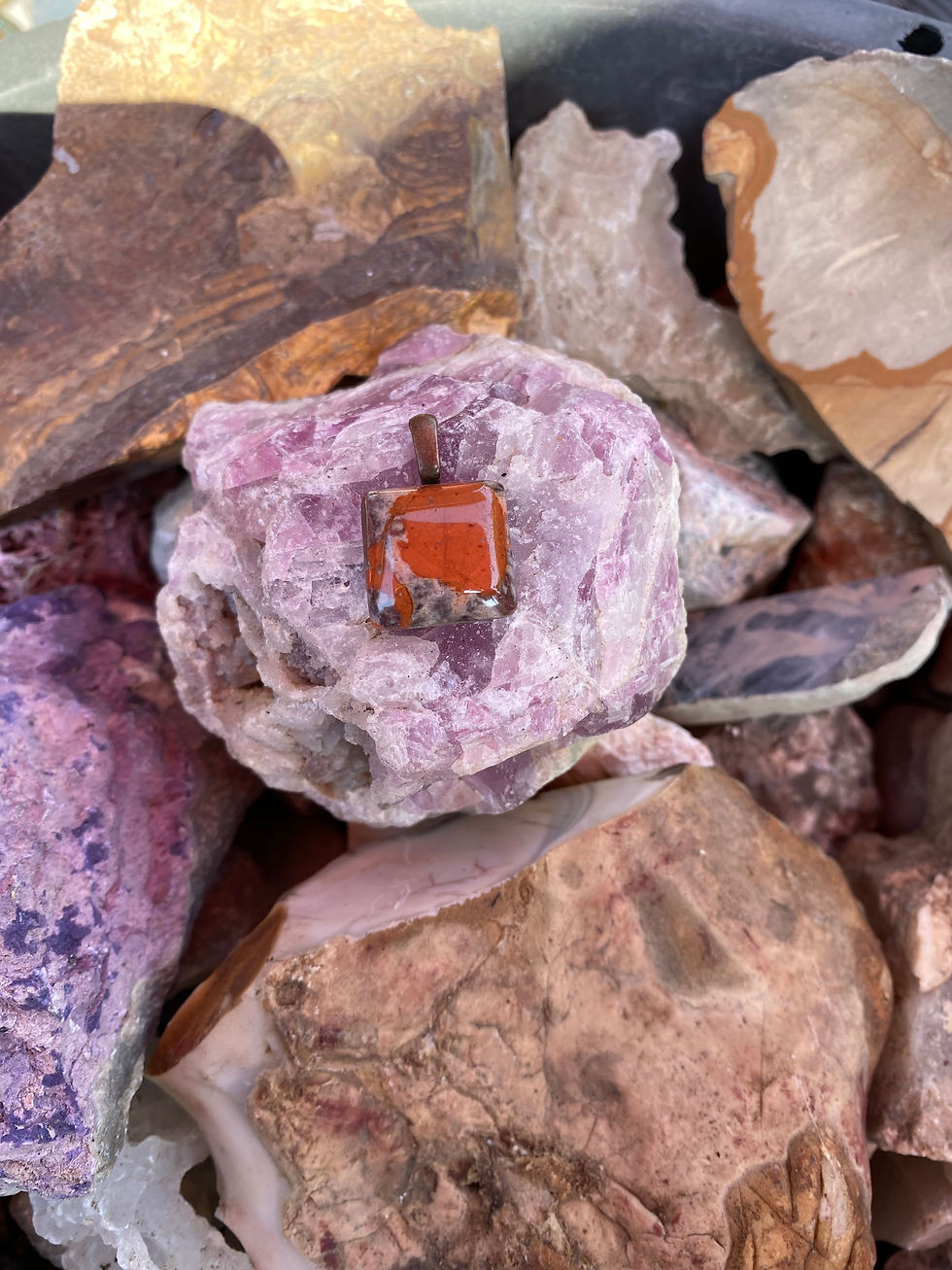 New Mexico Jasper on a brass bail pendant, resting on a bed of pink and purple gemstones.
