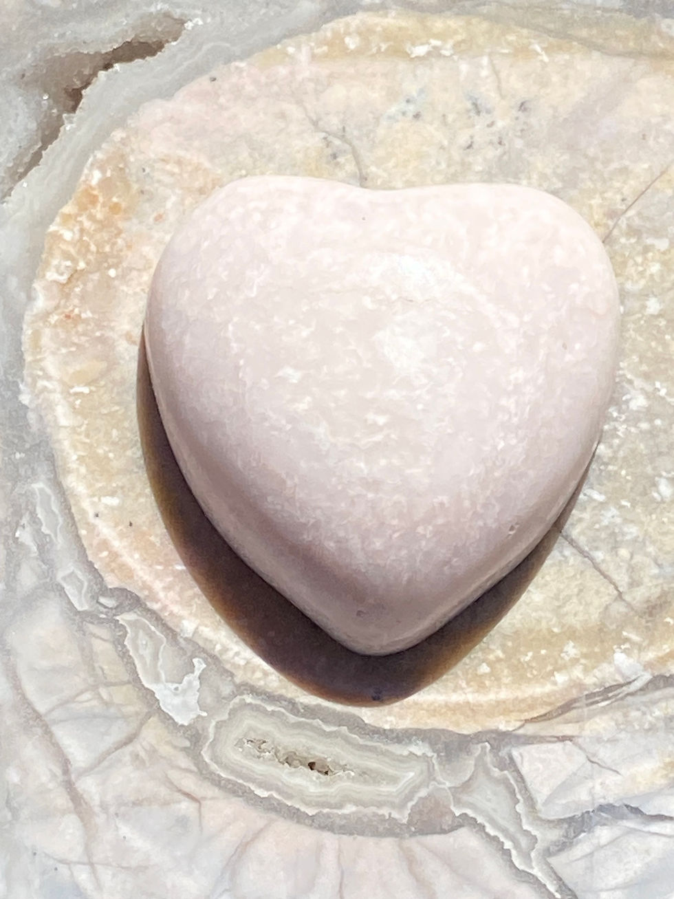Close-up of a polished Pink Opal heart stone on a textured agate background.