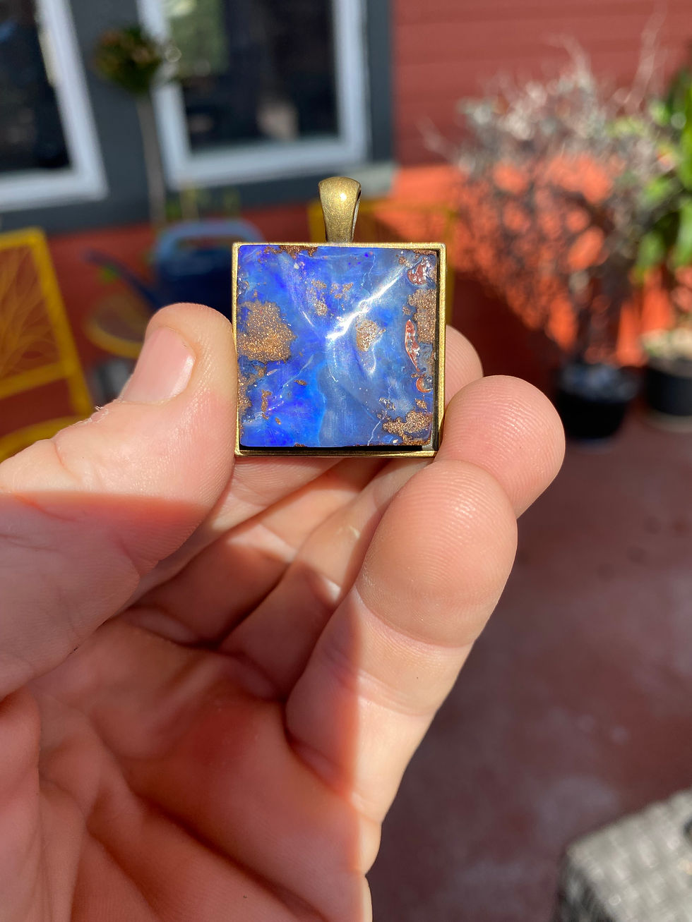 A close-up of the opal pendant nestled among raw stones, showcasing the dynamic interplay of swirling blues, purples, and ear