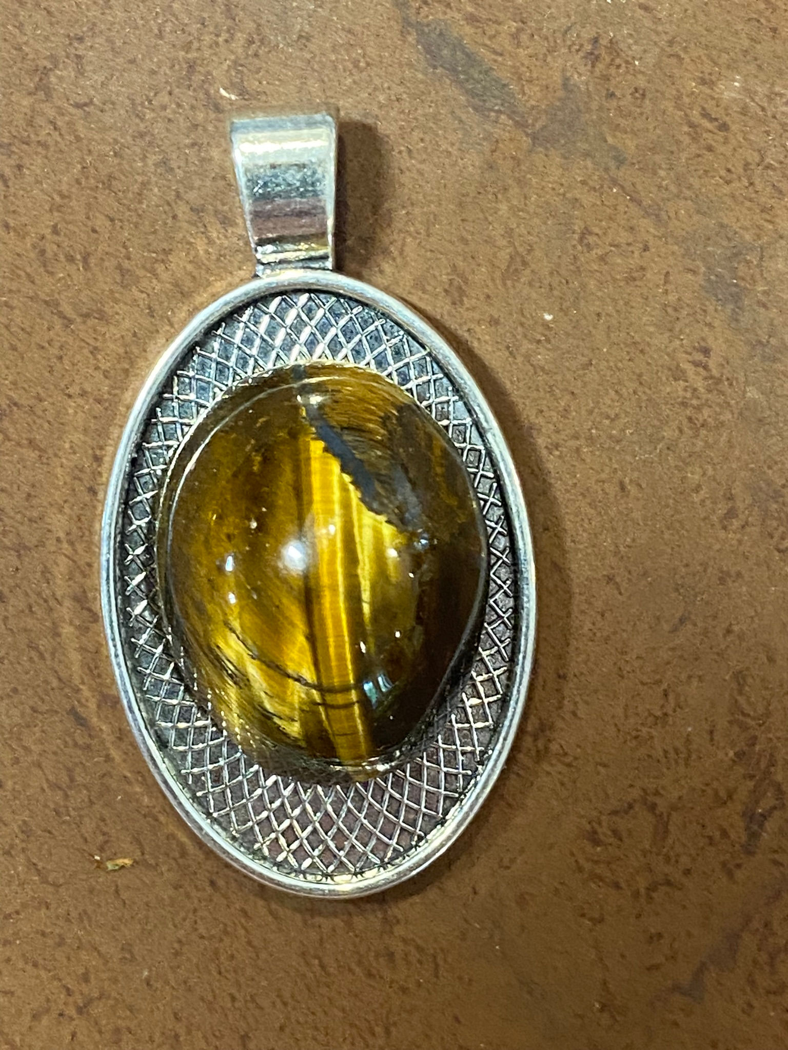 Close-up of Tiger Eye gemstone in an silver plated pendant setting on a pink crystal background.