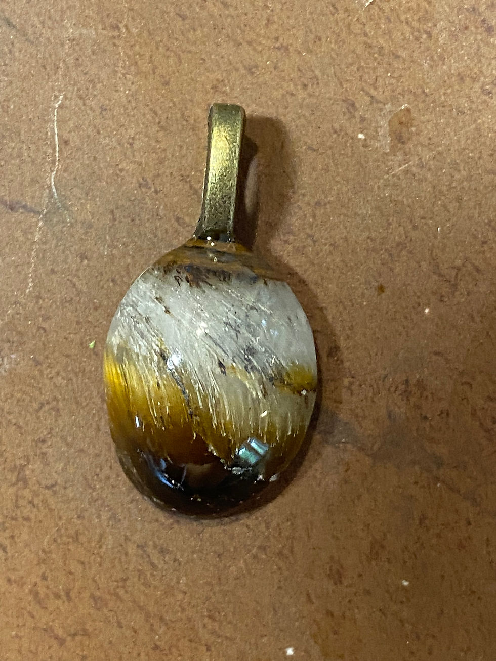Close-up view of a Oval Tiger Eye pendant on a leather cord with a bronze bail, displayed against a textured red backg