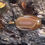 Thumbnail: Horizontal view of a banded agate pendant displaying its layered pattern, resting on a piece of textured driftwood.