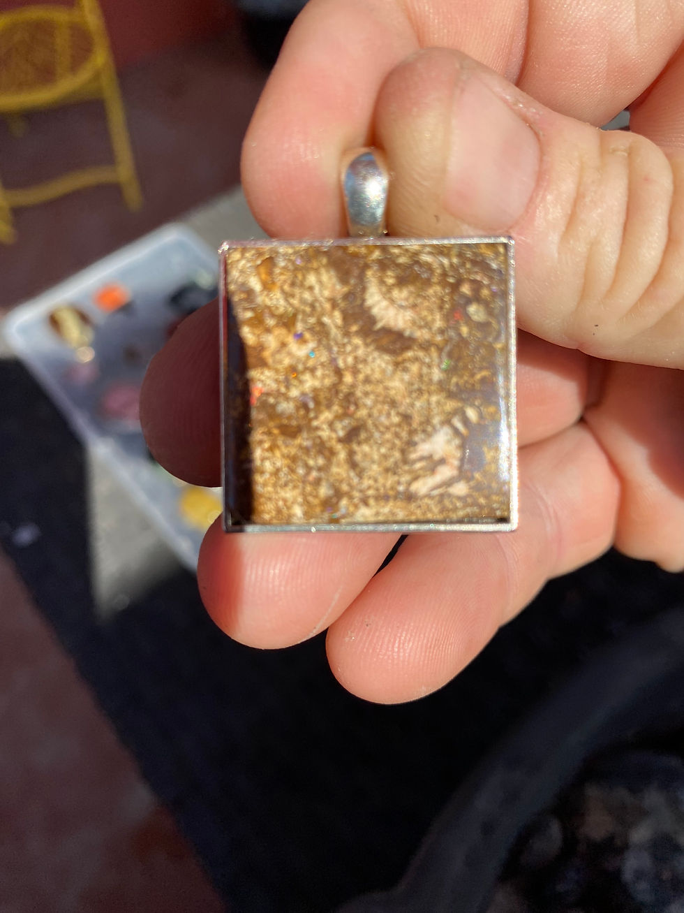 Hand holding a square Australian boulder opal pendant, highlighting its vibrant opal inclusions within a brown matrix.