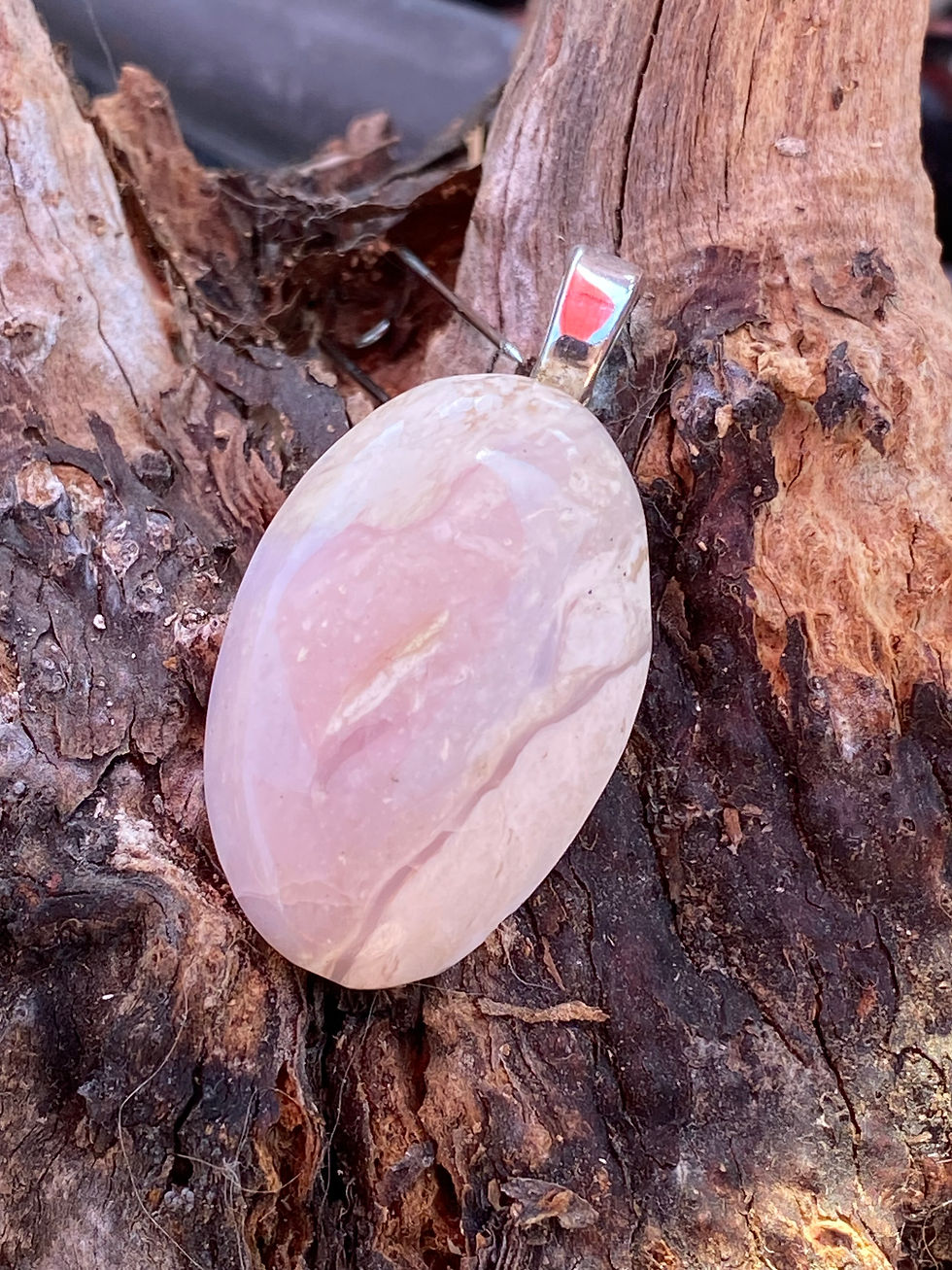 Vertical view of Pink Opal Pendant against a rustic background, highlighting its polished surface and silver bail.
