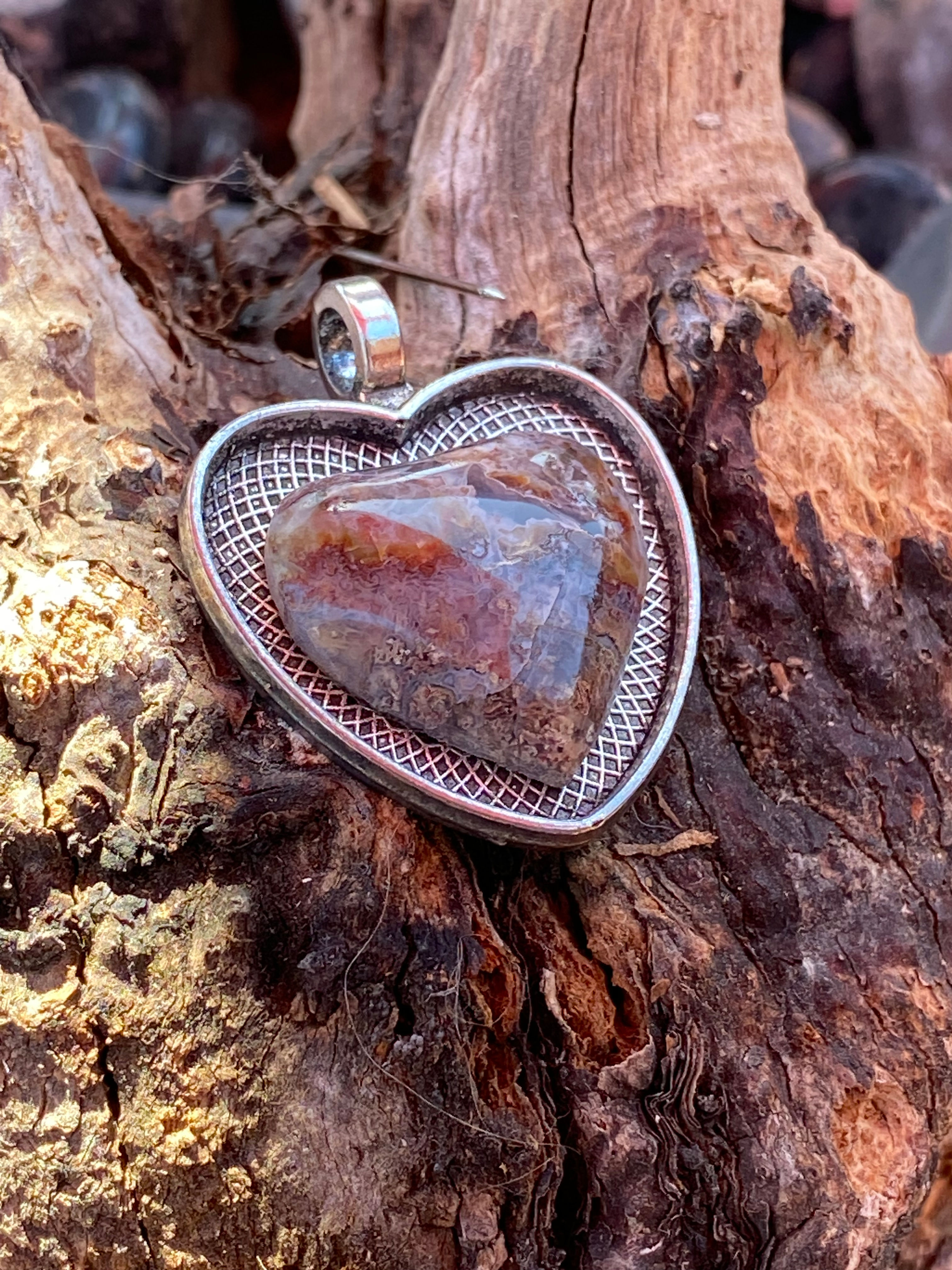Angled view of Butte Creek Agate Heart Pendant resting on wood, showcasing its unique gemstone and silver setting.
