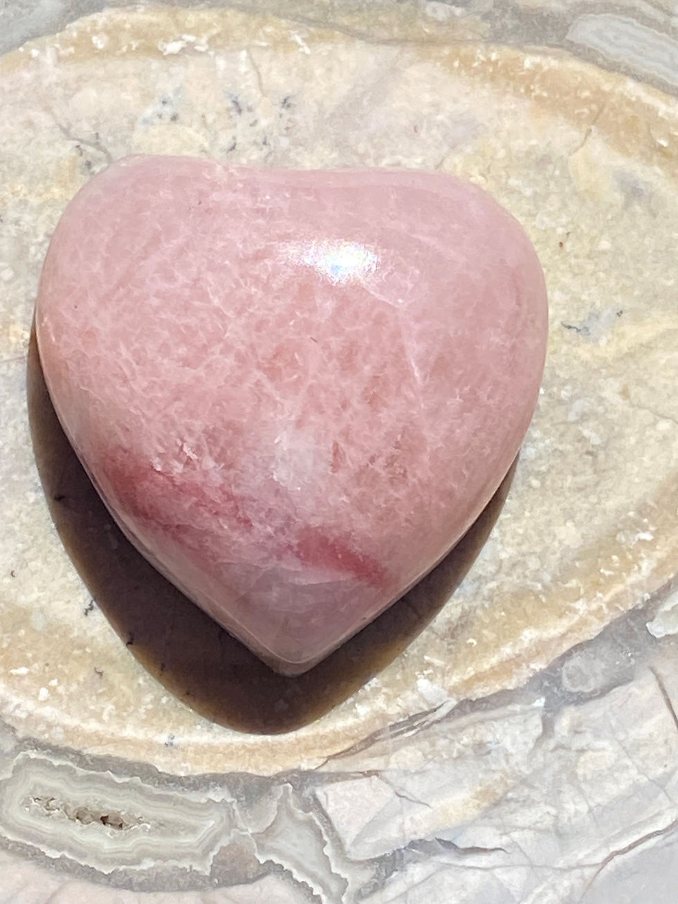 Pink Petalite heart-shaped gemstone displayed on a natural stone background.