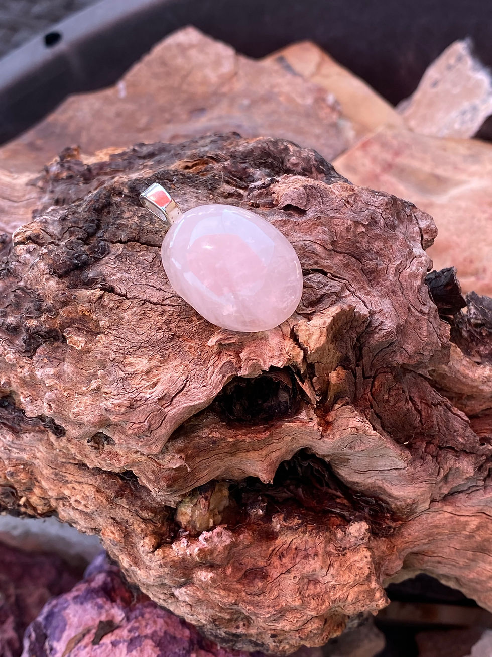 Angled view of Pink Petalite Pendant with sterling silver bail resting on rustic wood.