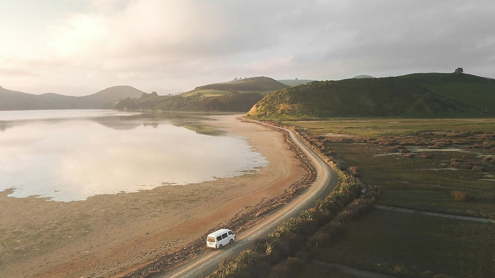 A campervan driving into the sunset along a beach