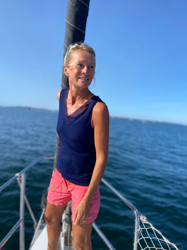 Marion Monnier standing at the bow of her sailing boat, radiating joy and fulfillment—embracing the freedom and balance of life at sea.