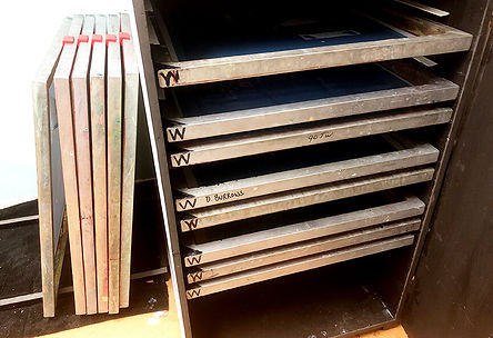 A pile of screens in a heated air drying cabinet with a stack of screens beside