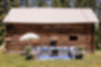 Outdoor wedding venue with old log cabin, flowing white flowers and fringed umbrella near Missoula, Montana ©"Wild Child" Photography
