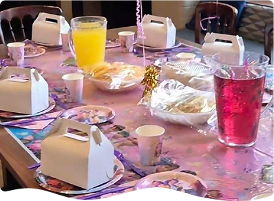 A table is decorated with baloons and a kids' tablecloth, set up for a childrens lunch box buffet