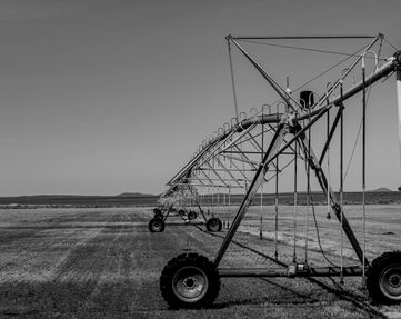 This is a picture of farming equipment i took in central oregon last year. it's used to water craps it's very long, has wheel's on the bottom, lots of different things hanging about to spray water over the crops. This image is in black and white.