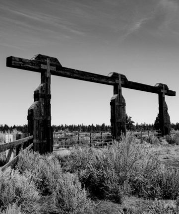this picture is of a huge wooden fence, crosses on the top, and is locked. it is in black and white.