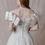 Thumbnail: Red haired model wearing vintage Amsale wedding dress with oversized off-shoulder sleeve against beige backdrop