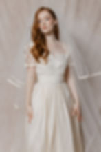 Red haired model wearing 1960s inspired silk wedding dress against beige backdrop