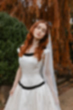 Thumbnail: Red haired model wearing black and white vintage Vera Wang wedding dress standing near a tree with orange leaves
