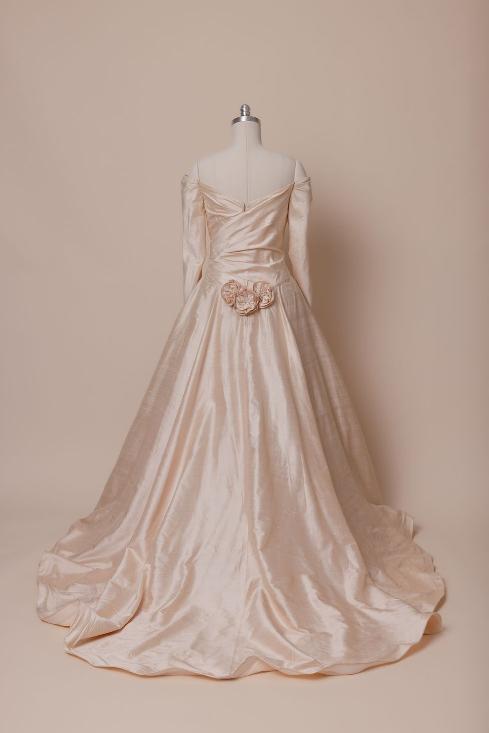 Thumbnail: Back of pink silk off-shoulder long-sleeved vintage wedding dress with rosettes against a beige backdrop