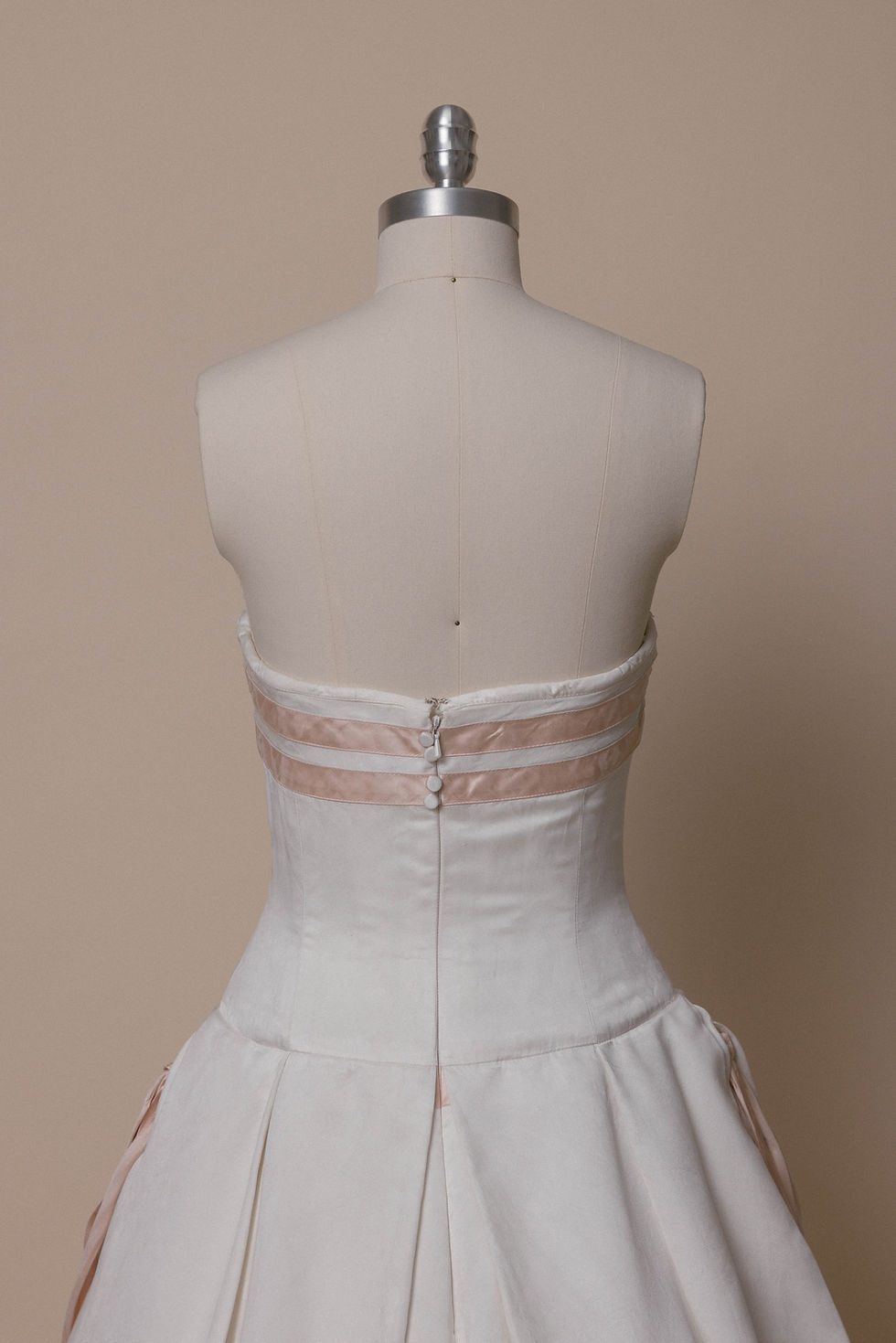 Thumbnail: Vintage Carolina Herrera wedding dress with pink accents on dress form against ivory backdrop