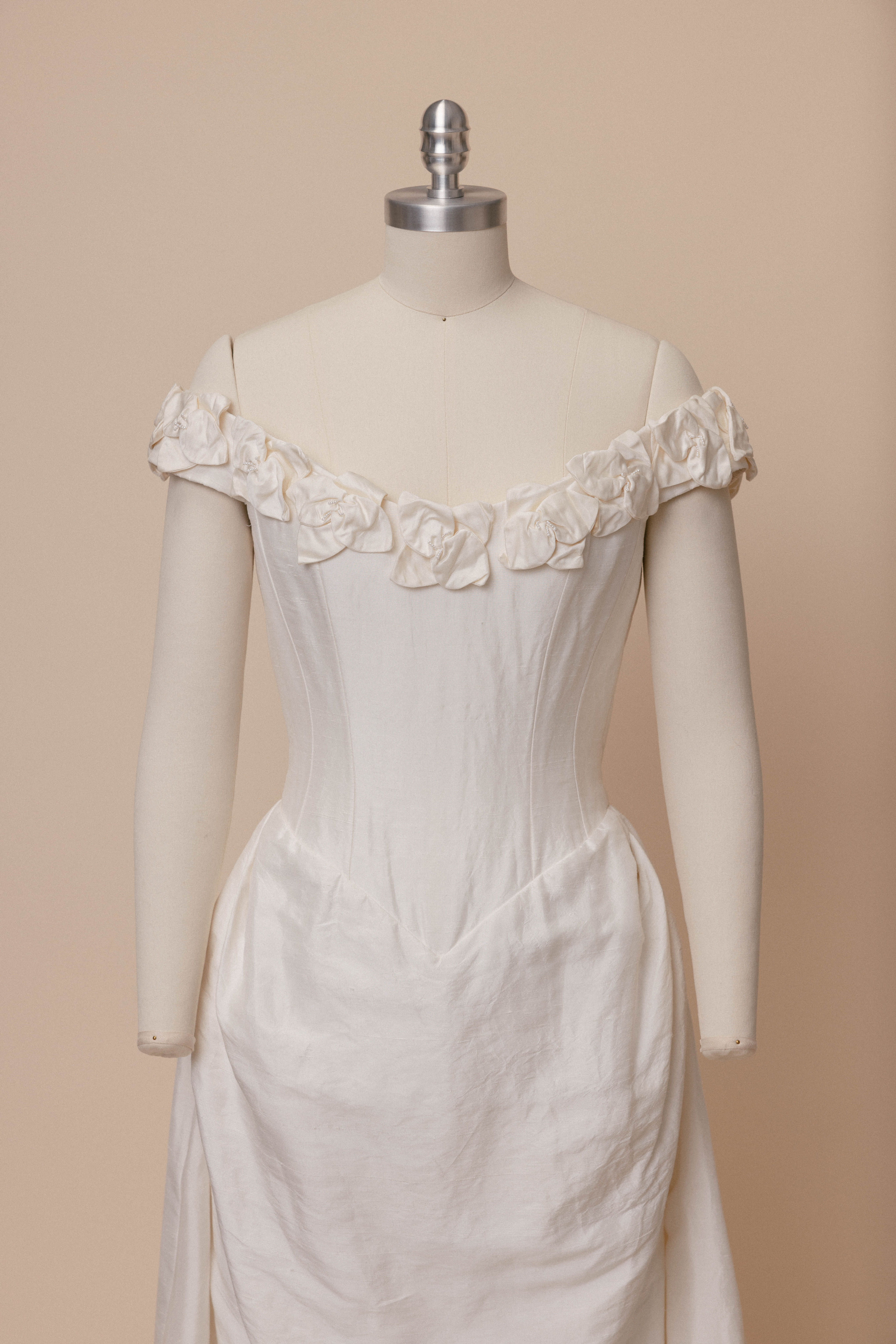 The Catherine Rayner Lily wedding dress with floral neckline on a dress form against an ivory backdrop