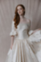 Red haired model wearing Renaissance inspired vintage wedding dress with off shoulder sleeves against beige backdrop