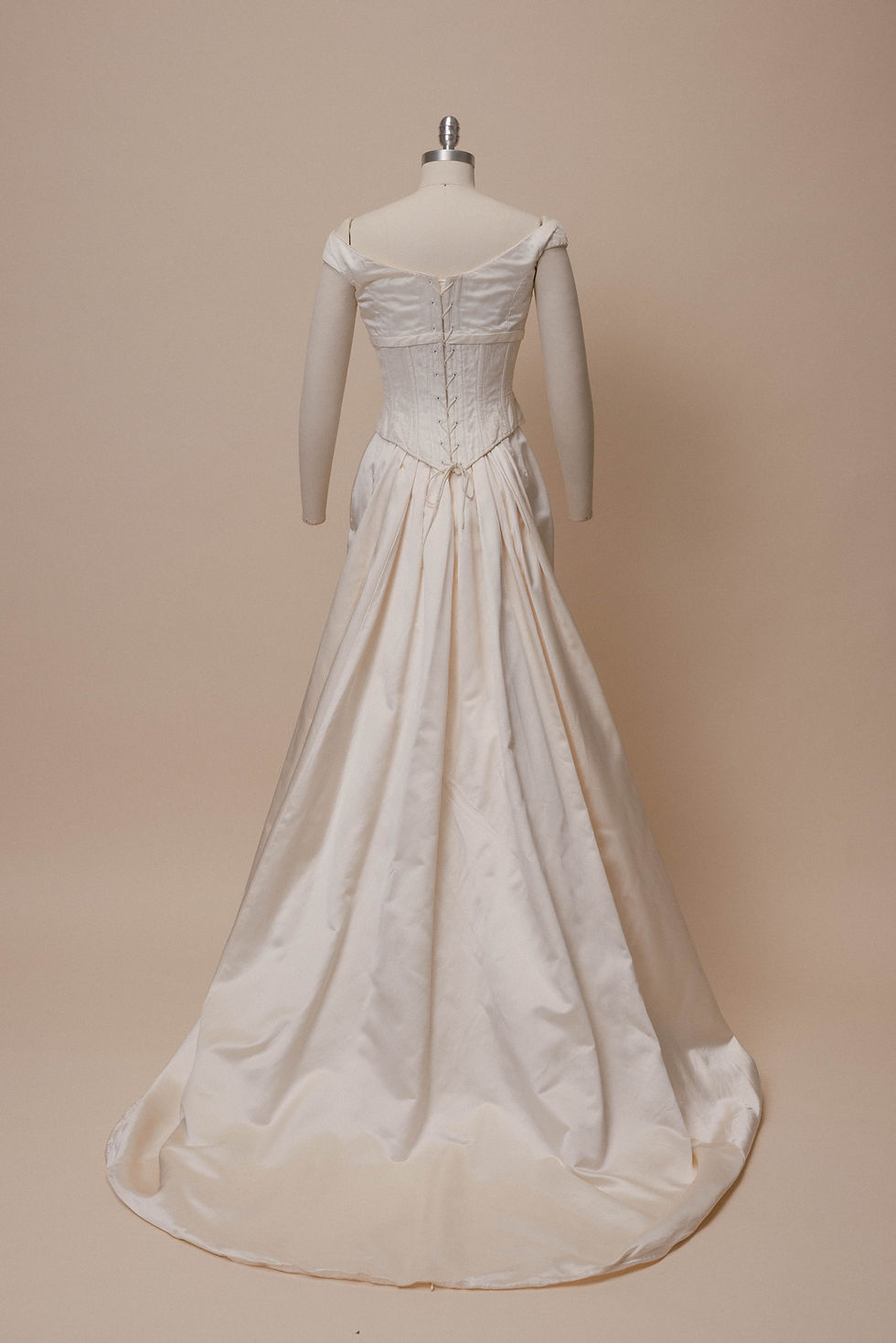 Thumbnail: Red haired bride wearing vintage silk corset wedding dress and standing against an ivory backdrop