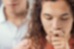 A person with a facial piercing appears to be experiencing anxiety, covering their mouth with a hand as another individual offers support in the background.