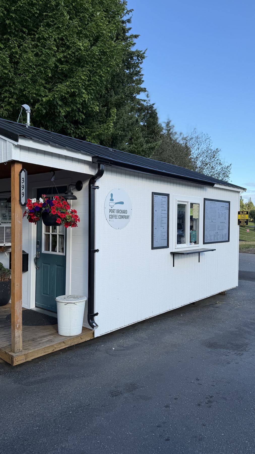 The Port Orchard Coffee Company stand: a white building with a teal door, hanging flowers and the menu boards beside the order window